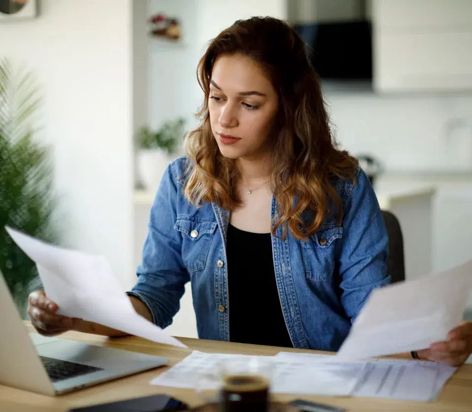Woman with brown hair wearing a blue long sleeve shirt, sat at a table, looking at paperwork