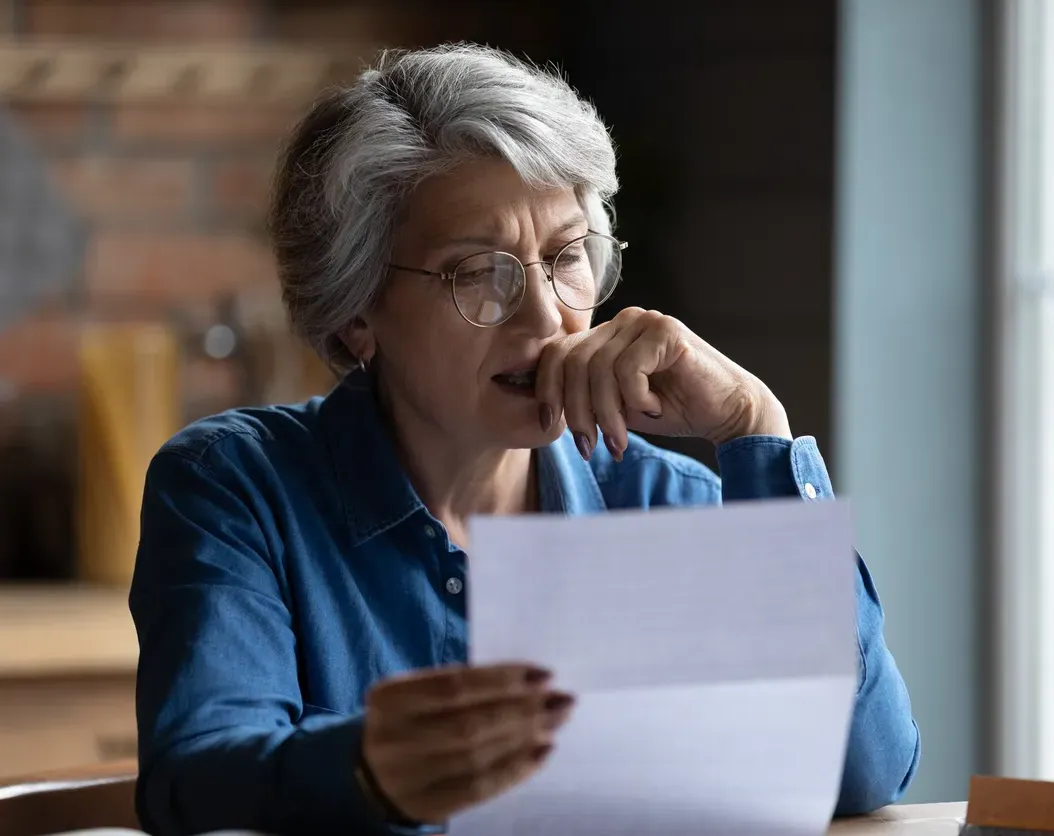 Concerned Woman sitting at a desk looking over paperwork wearing a blue long sleeved shirt.